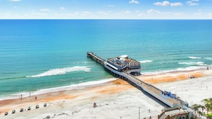 Eine Pier, die sich ins Meer erstreckt, mit einem Gebäude am Ende, neben einem Sandstrand.