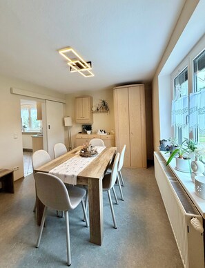 Una cocina moderna con comedor, armarios de madera y un ventanal con plantas.
