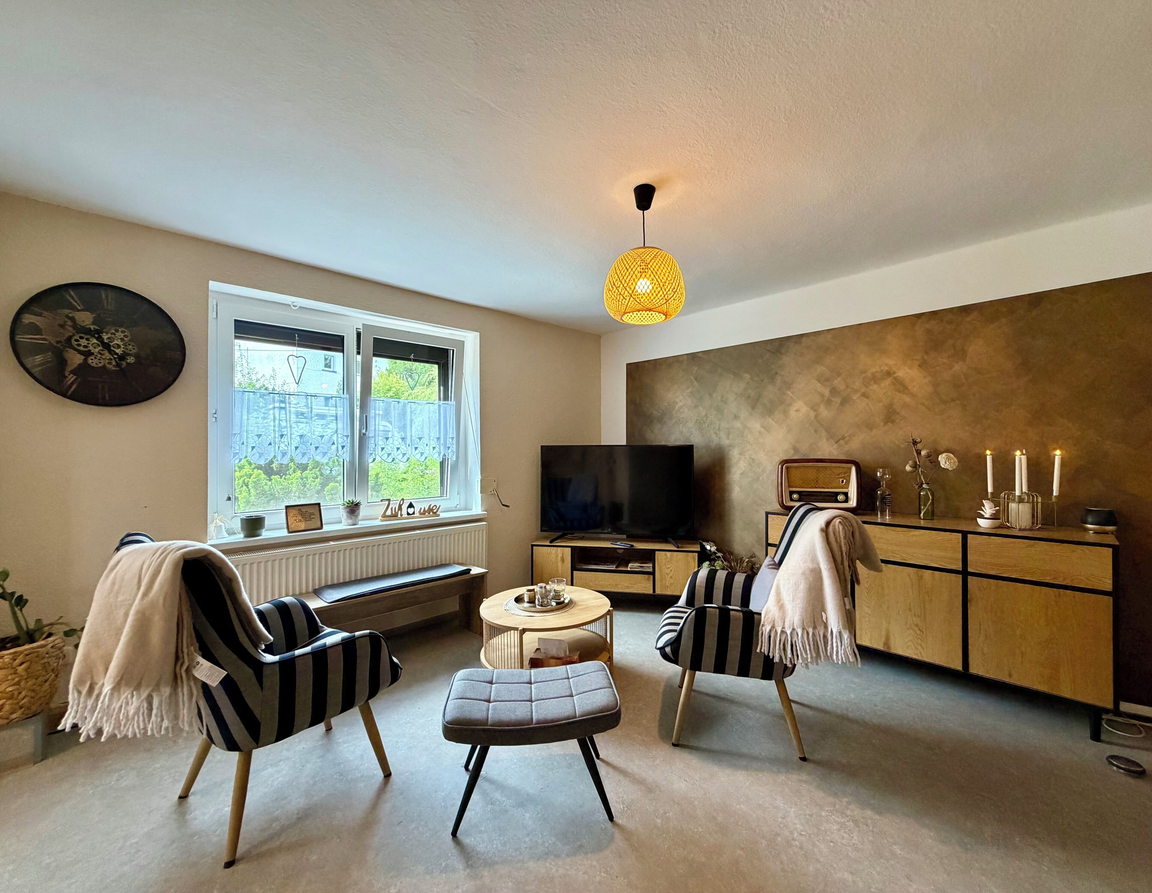 Uma sala de estar com televisão, radiador, janela com vista, sofá, mesa de centro e um armário com velas.