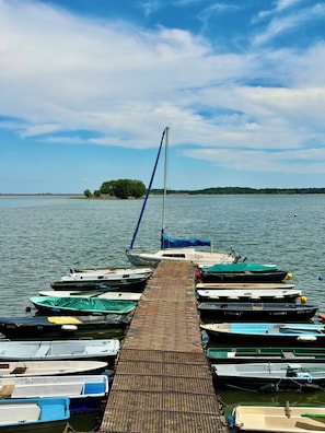 Un muelle con varias embarcaciones amarradas, cielo despejado y una costa distante.