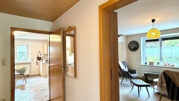Een ruime woonkamer met houten plafond, grote spiegel, eettafel met stoelen en uitzicht op het landschap door een raam.