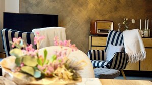 Ett modernt vardagsrum med en platt-TV, en randig fåtölj, en gammal radio och en dekorativ vas med blommor.
