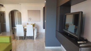 A modern living room with a flat-screen TV, a dining area with white chairs, and a green sofa. - Apartment Villamartin (Orihuela Costa)