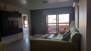 A living room with a sofa, a coffee table, and a TV. There is a sliding glass door leading to an outdoor area. - Apartment Villamartin (Orihuela Costa)