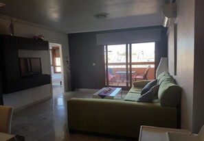 Ein Wohnzimmer mit einer Couch, einem Couchtisch und einem Fernseher. Eine Glastür führt zu einem Außenbereich.