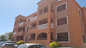 A multi-story building with balconies, a parking lot, and a clear sky. - Apartment Villamartin (Orihuela Costa)