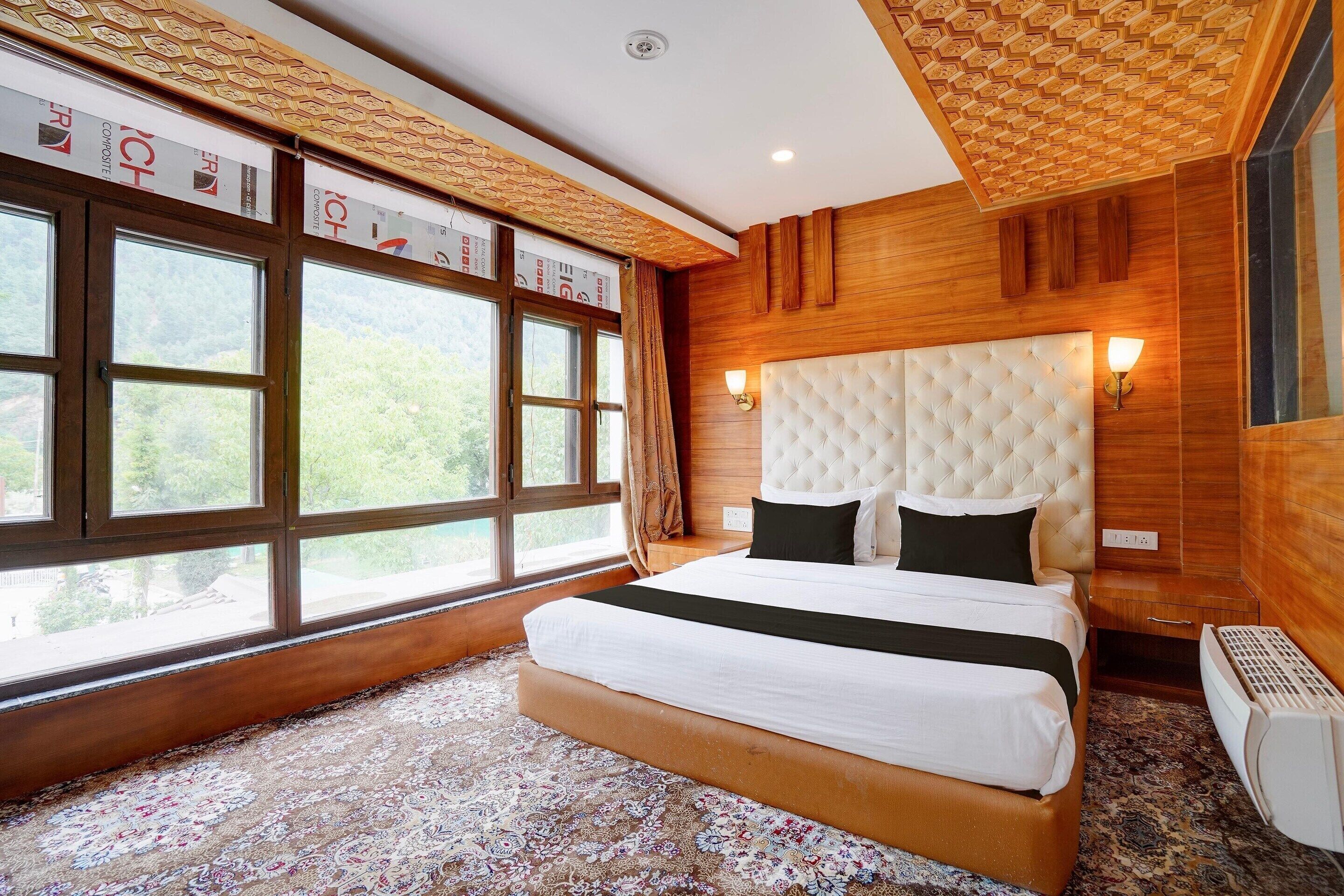 A bedroom with a large window, a tufted headboard, and a patterned carpet.