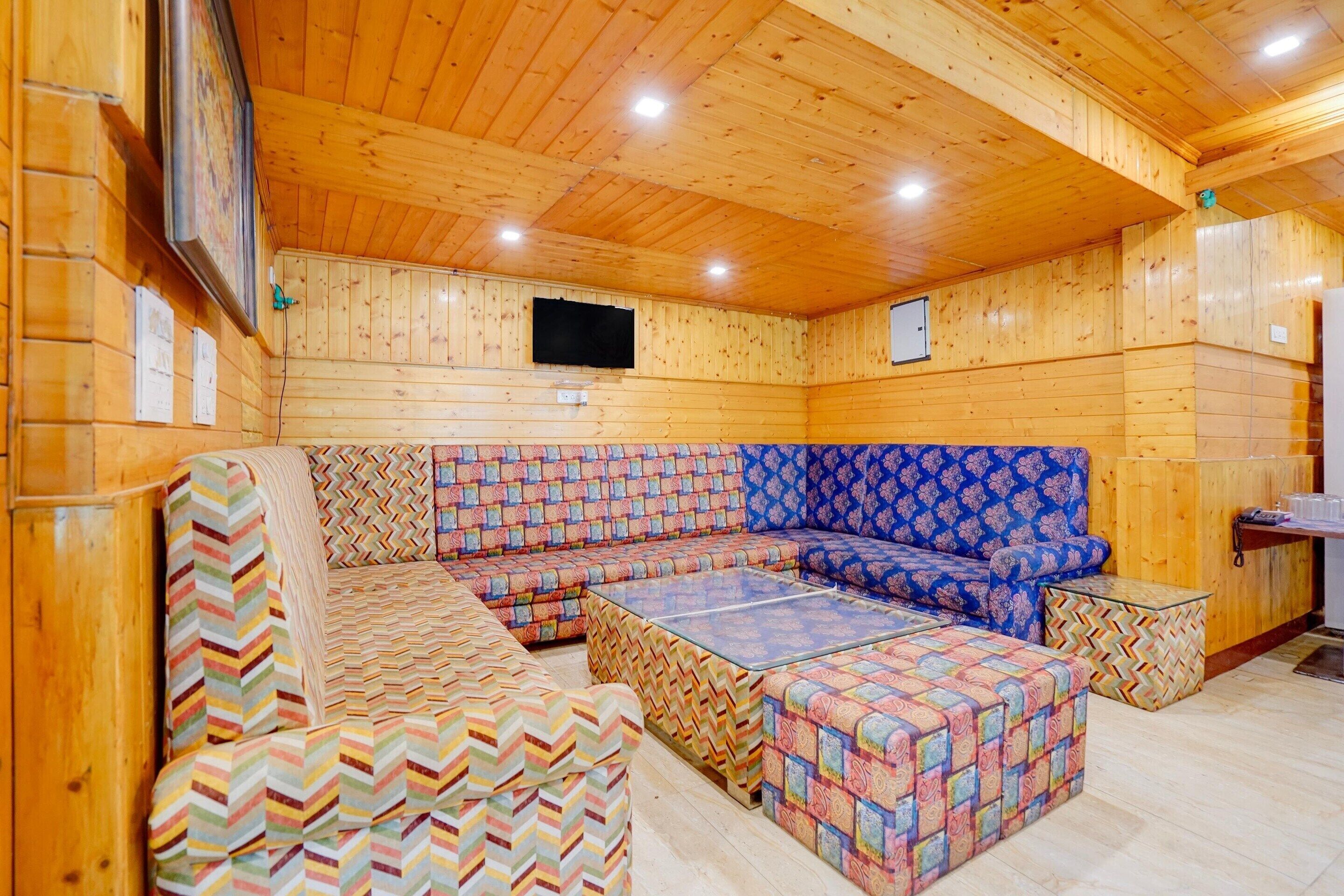 A wooden interior with a sectional sofa, a patterned ottoman, and a flat-screen TV mounted on the wall.