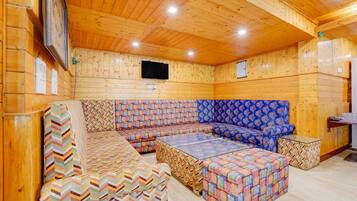 A wooden interior with a sectional sofa, a patterned ottoman, and a flat-screen TV mounted on the wall.