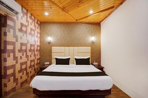 Habitación de hotel con una cama grande, techo de madera, paredes estampadas y dos lámparas de noche.
