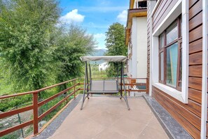 Un balcón con barandilla de metal, una mesa con toldo y vistas a zonas verdes y montañas.