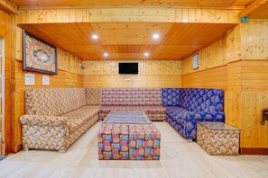 Un interior de madera con un sofá y reposapiés, un televisor de pantalla plana montado en la pared, y una obra de arte floral enmarco.