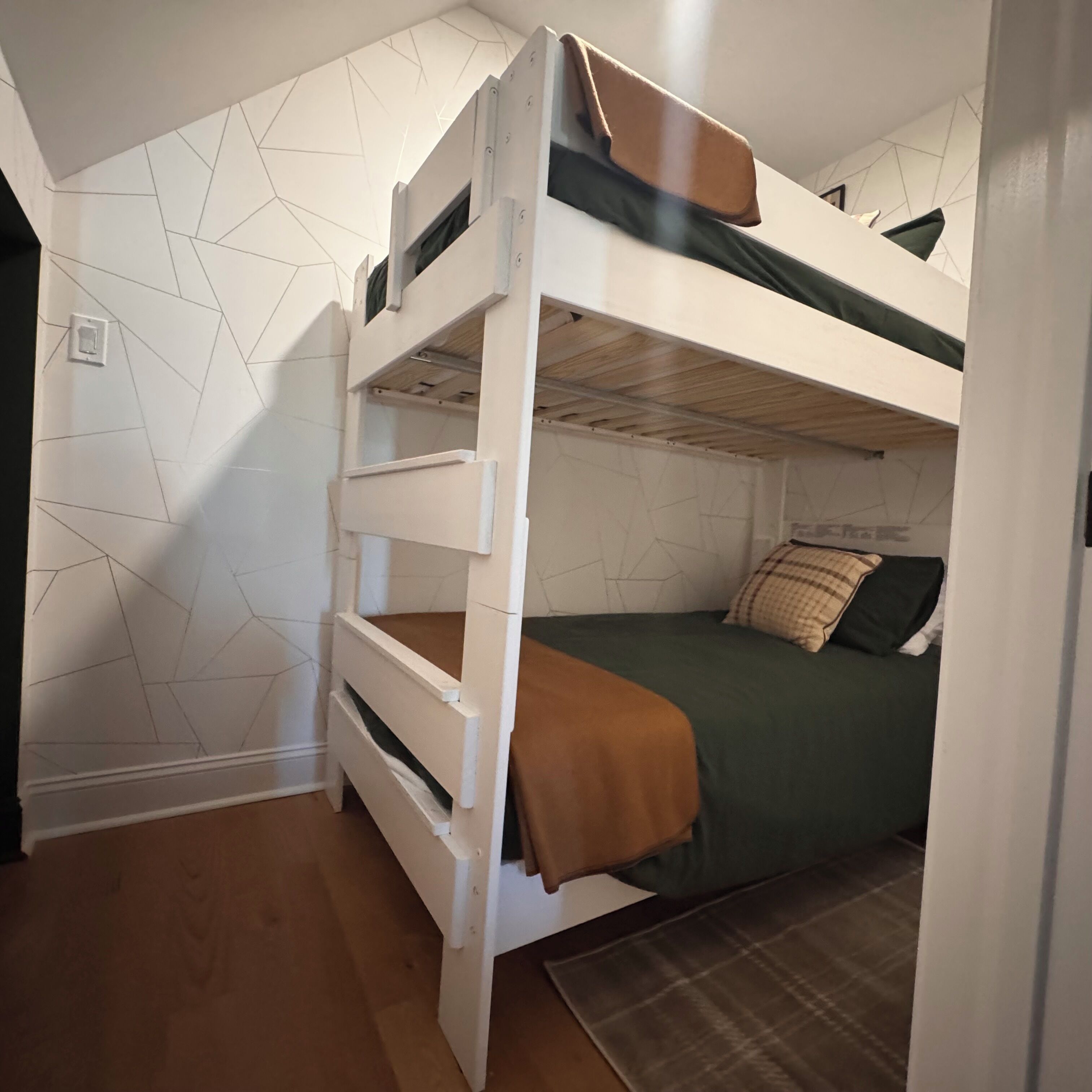 A bunk bed room with a geometric wall pattern, a wooden floor, and a green bedspread.