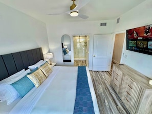 A hotel room with a bed, a ceiling fan, a TV mounted on the wall, and a door leading to a bathroom. - Balcony Lake Views |  Pool, Gym, WiFi & Parking (Orlando)