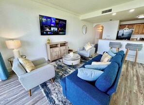 Een moderne woonkamer met een televisie, banken, een salontafel en een keuken op de achtergrond.