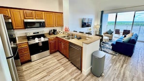 A modern kitchen with wooden cabinets, stainless steel appliances, and a large island. There is a balcony with a view of the ocean. - Balcony Lake Views |  Pool, Gym, WiFi & Parking (Orlando)