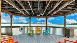 A covered deck with a view of the sea, featuring a ceiling fan, and three colorful Adirondack chairs. - Balcony Lake Views |  Pool, Gym, WiFi & Parking (Orlando)