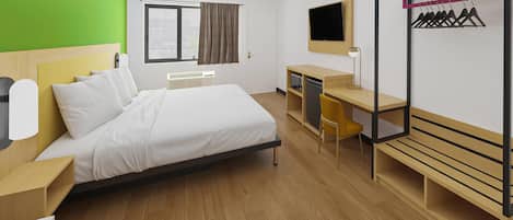 A hotel room with a bed, desk, chair, and a coat rack with hangers.