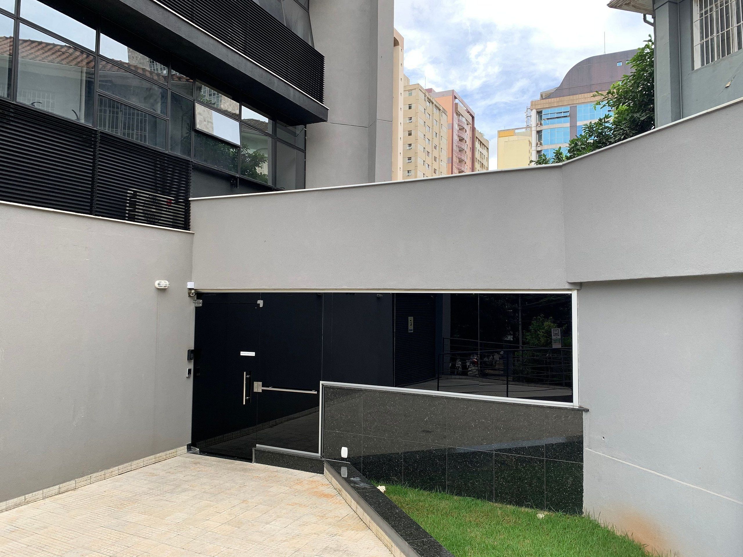 Un edificio moderno con una puerta de entrada negra, un ventanal de vidrio y una barandilla metálica.