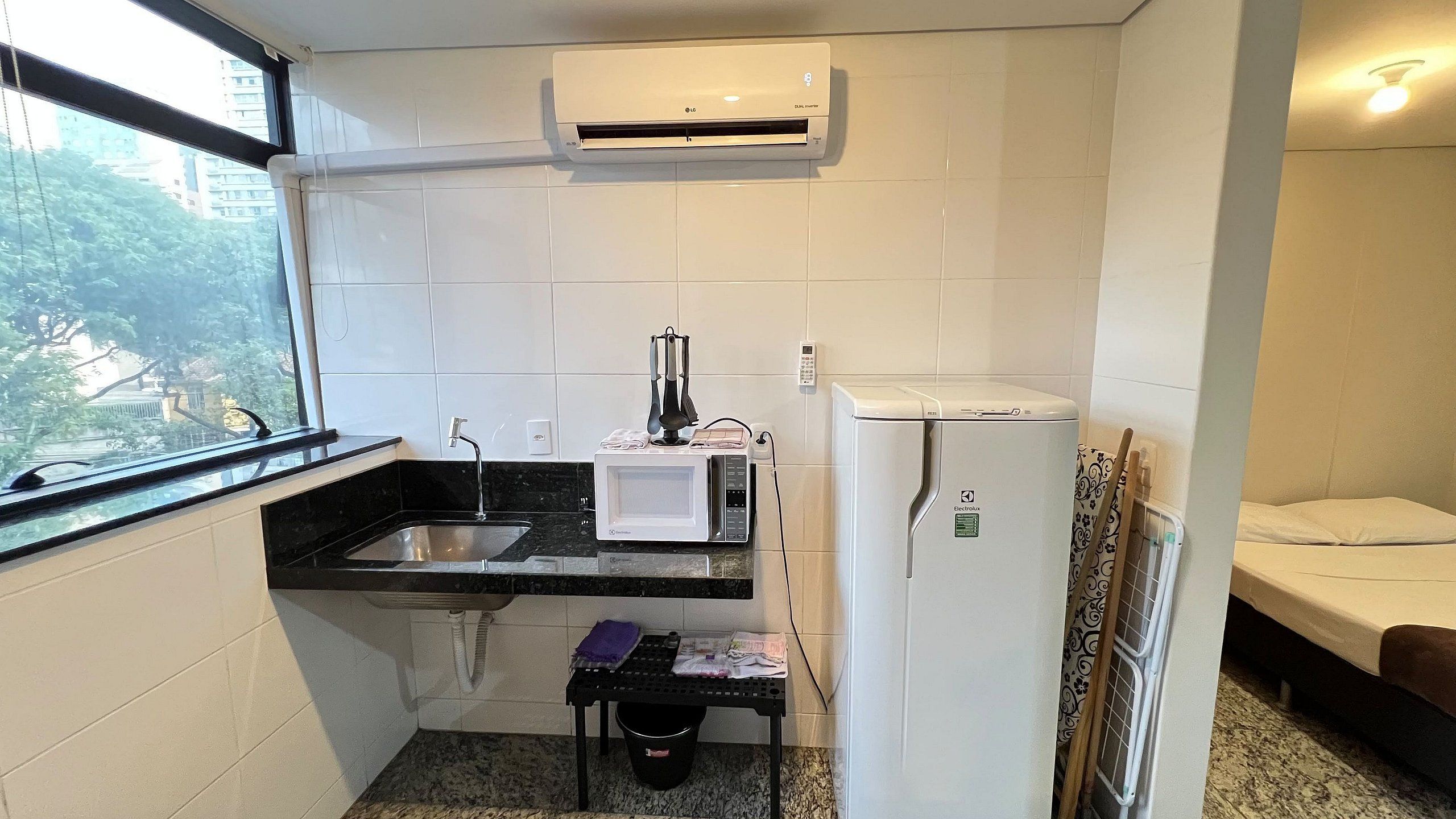 A compact kitchen with a sink, a microwave, a refrigerator, and a window with a view of buildings outside.
