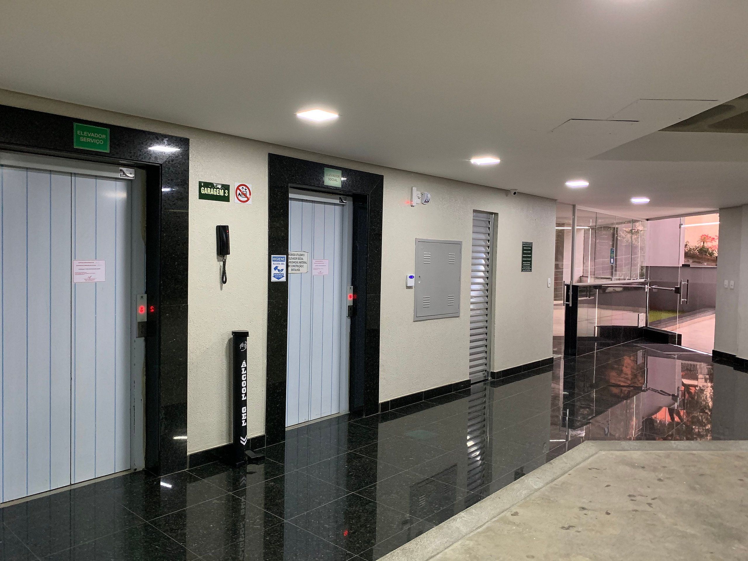 A clean, well-lit hallway with a polished floor, an elevator, and a door marked 'GARAGEM 3'.