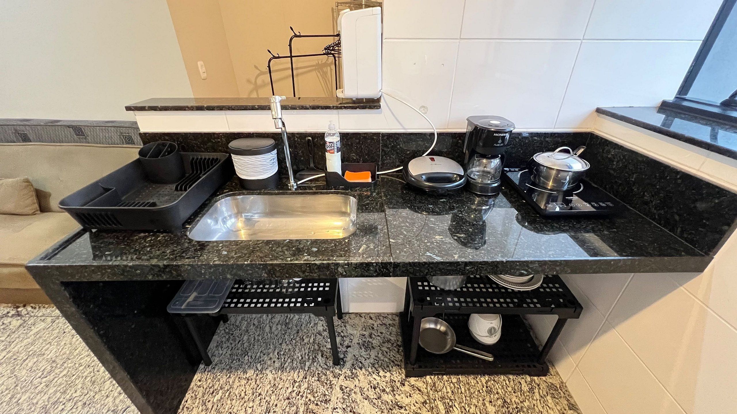 A kitchen with a black countertop, a sink, a stove, and various kitchen utensils.