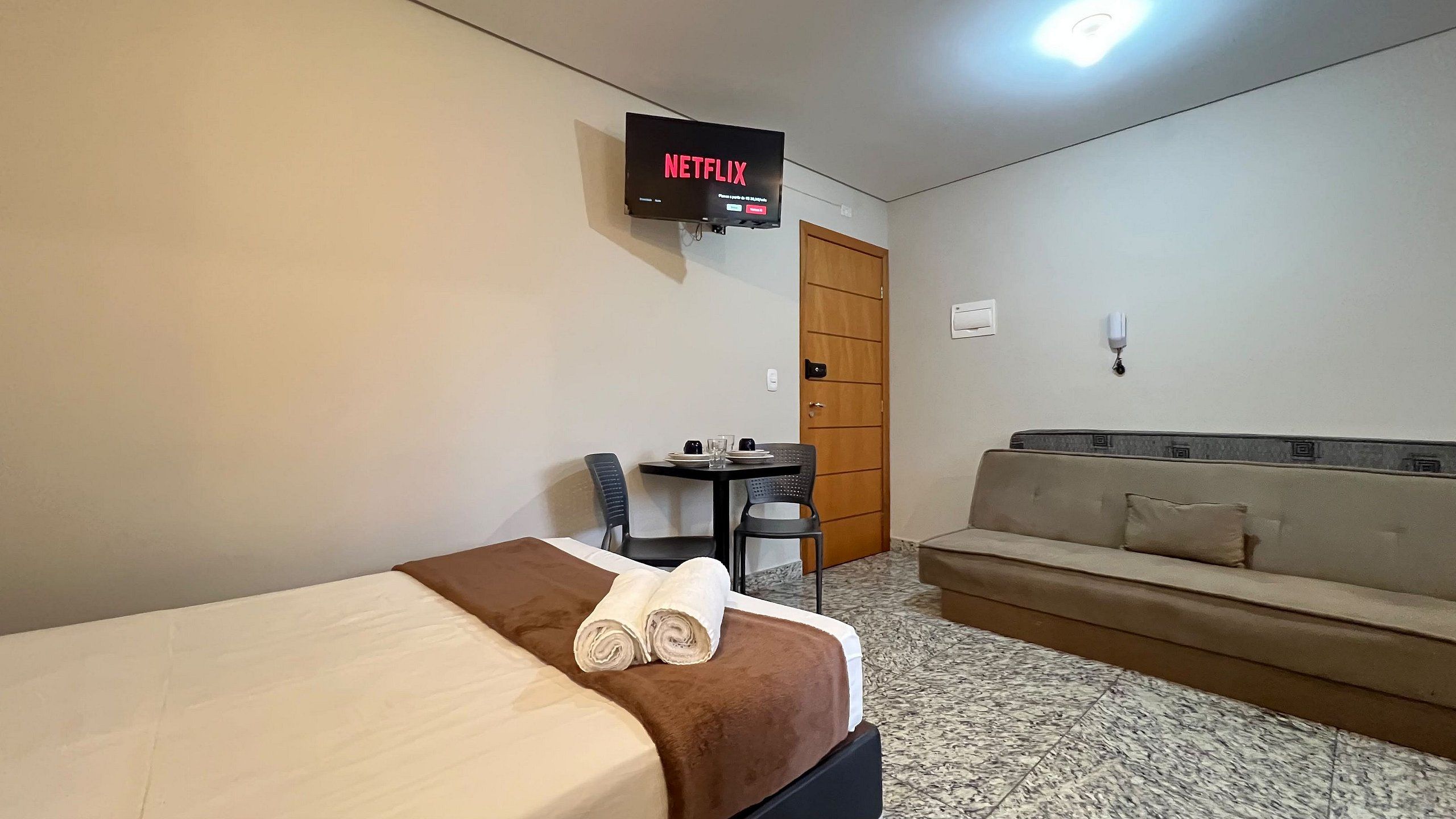Habitación de hotel con cama, sofá, escritorio con silla y televisor mostrando el logotipo de Netflix.