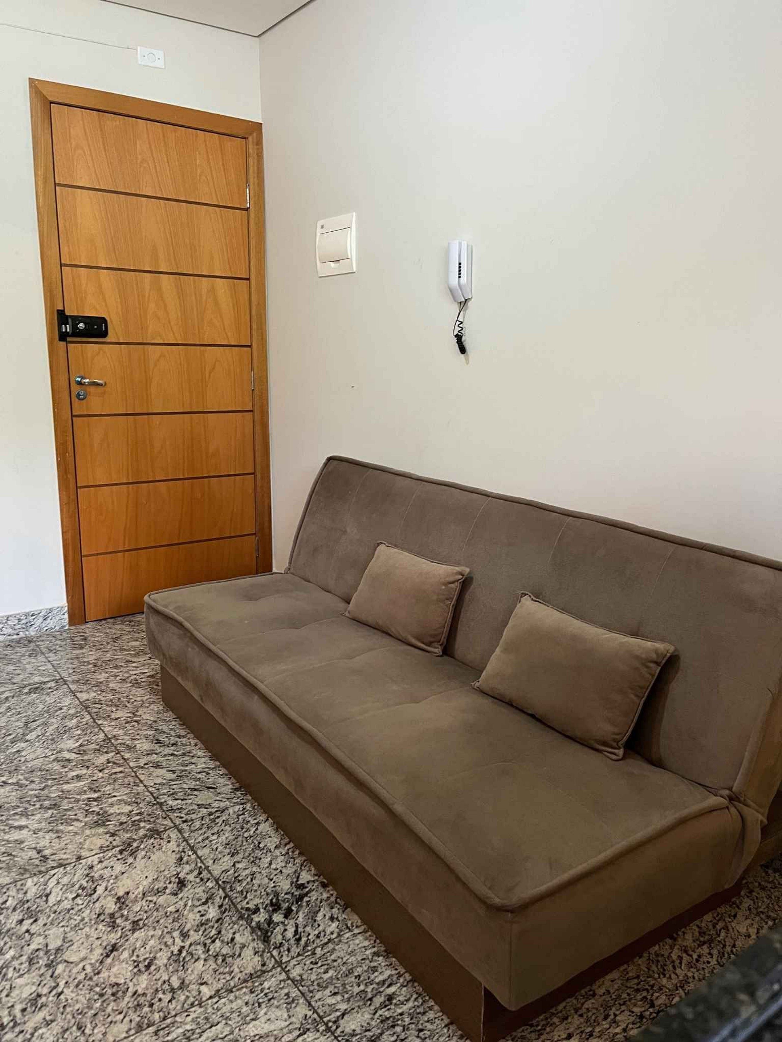 Ein Zimmer mit Holztür, einer Couch, einem Wandtelefon und einem Fliesenboden.