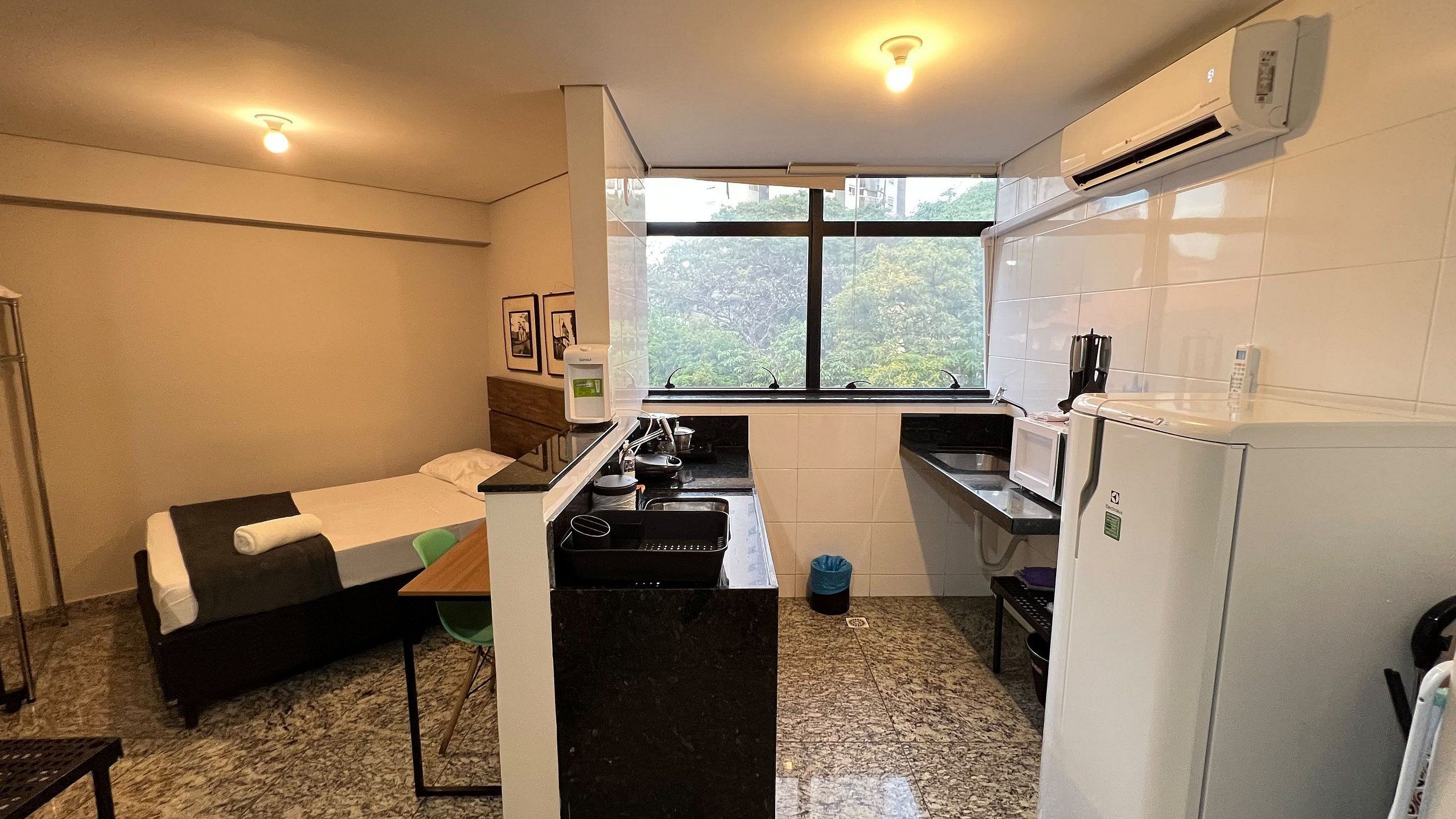 Habitación compacta con cama, kitchenette y ventana con vista a zonas verdes.