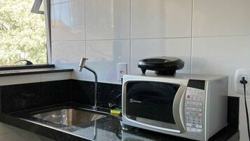 Una cocina con microondas integrado, un lavamanos de acero inoxidable y una ventana con persianas.