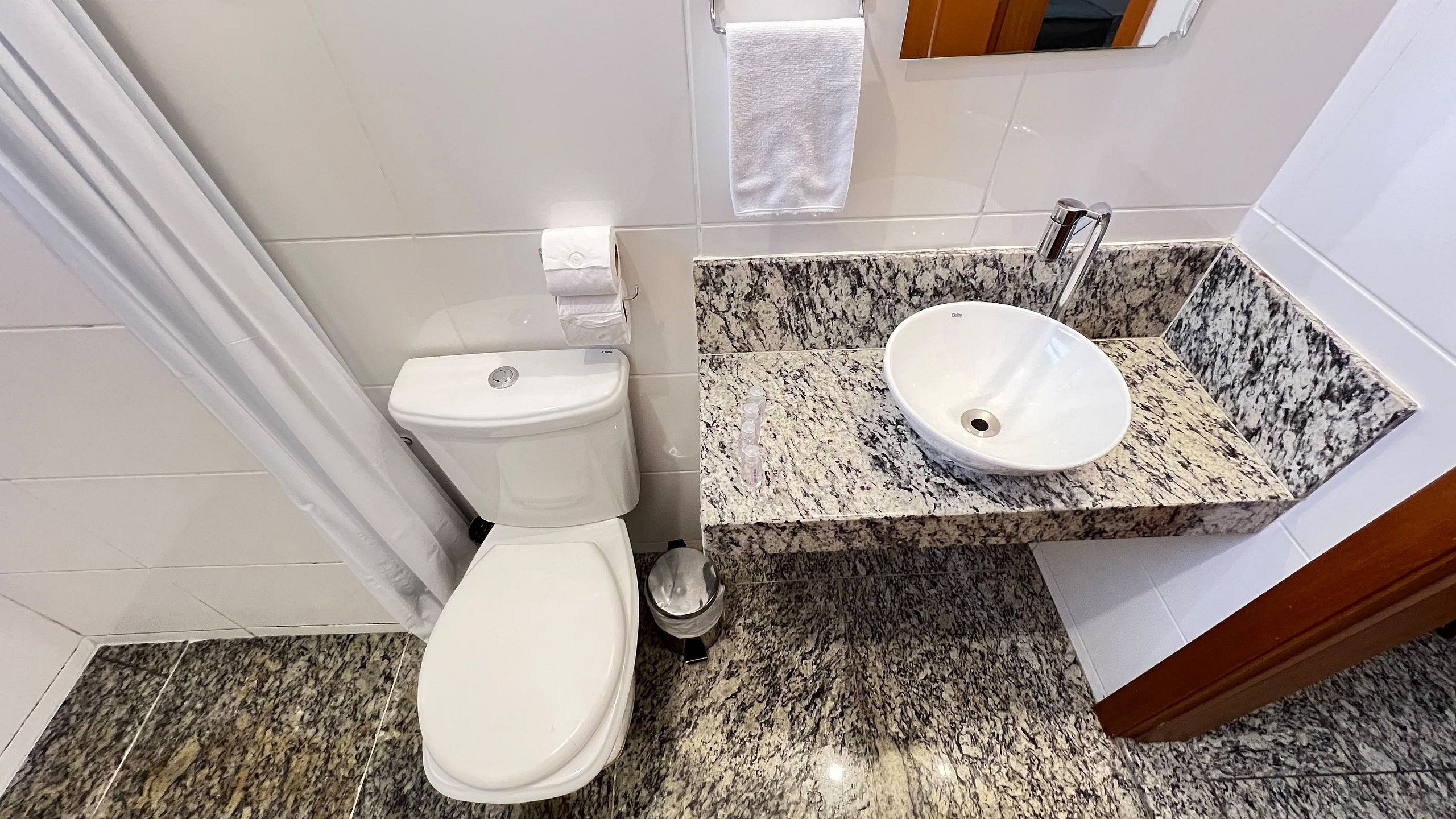 A bathroom with a white toilet, a granite countertop sink, and a marble floor.