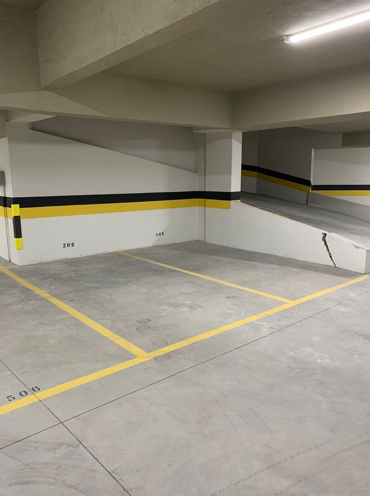 Un estacionamiento vacío con pisos de concreto, líneas pintadas en amarillo y negro, y una escalera.