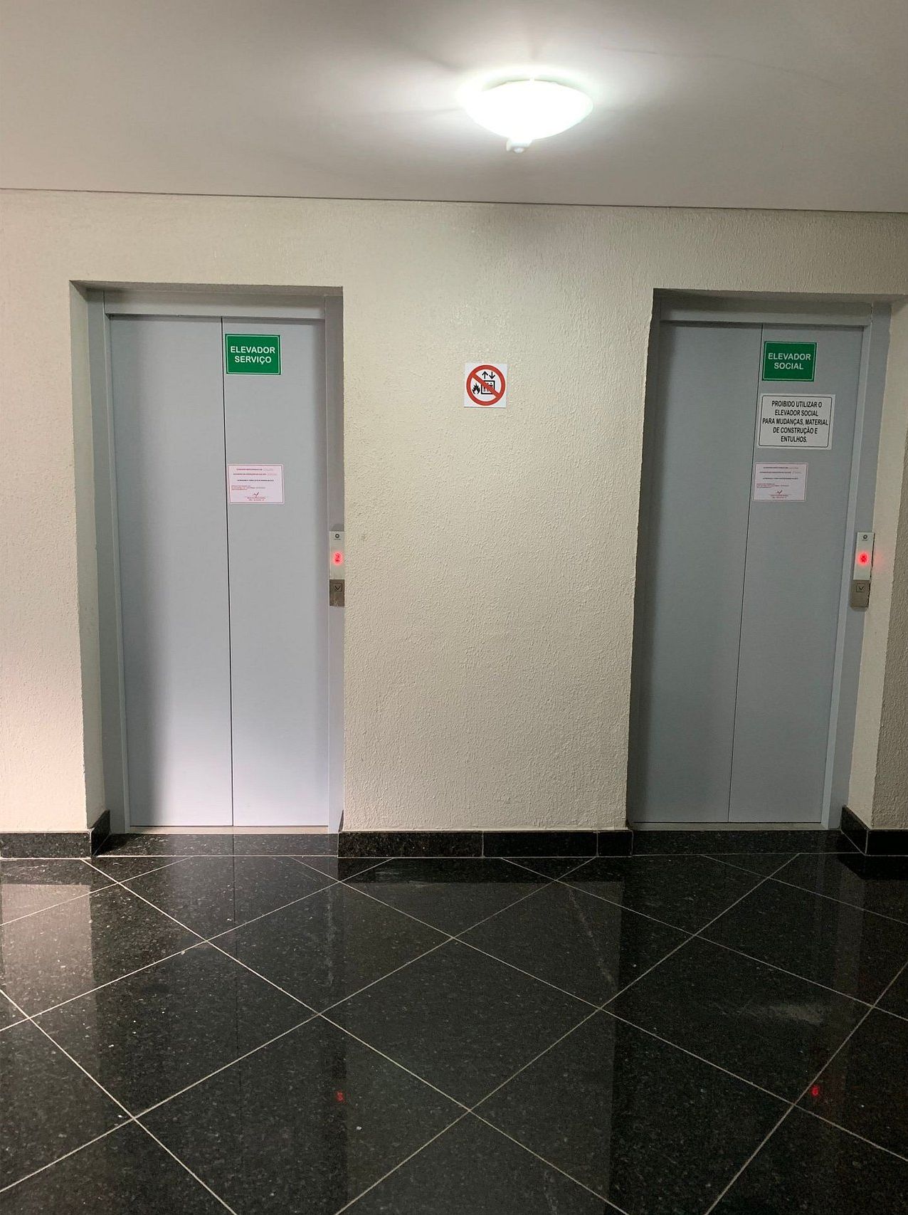 Dos puertas de ascensor con carteles de servicio y ascensor social, un letrero de prohibición de fumar y una advertencia sobre materiales de construcción.