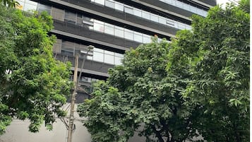 Un edificio moderno de varios pisos, con amplios ventanales y un estacionamiento con automóviles.