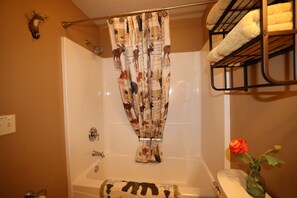 Baño con cortina de ducha, bañera, toallero y un florero con una flor.
