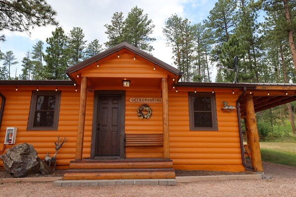 Una cabaña de troncos con puerta principal, una corona decorativa y un cartel que dice 'Deer Crossing'.
