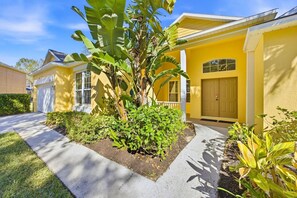 A yellow building with a garage, a front door, and a small porch with plants. - Dreamers Retreat! Spacious Disney-Area Pool Home for Families & Adult Getaways (Kissimmee)