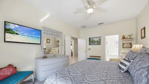 Une chambre à coucher avec un lit, une commode et un téléviseur diffusant une scène de plage.