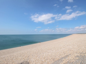 A wide, pebbled beach with a clear sky and calm sea. - Tipsy Turtle (Portland)
