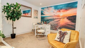 A room with a desk, a chair, a potted plant, a sofa with a patterned pillow, and a large beach sunset mural on the wall. - Tipsy Turtle (Portland)
