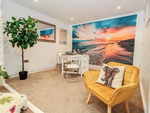 A room with a desk, a chair, a potted plant, a sofa with a patterned pillow, and a large beach sunset mural on the wall. - Tipsy Turtle (Portland)