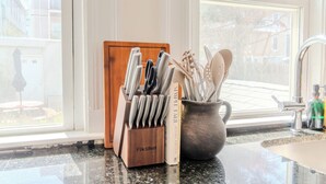 Een keuken met een messenblok, een mok met bestek en een raam met uitzicht op gebouwen.