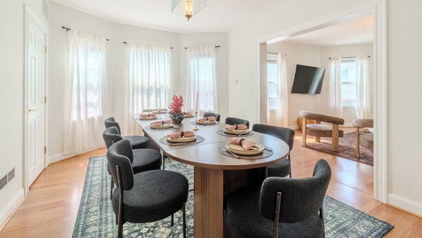 Een eetkamer met een ronde tafel, stoelen en een kroonluchter.