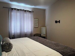 A bedroom with a bed, a chair, a mirror, and a wall-mounted light fixture. - perfect stay in best small town (Somerton)