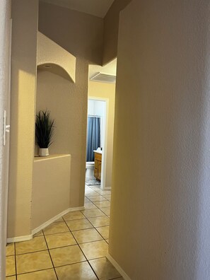 A hallway with beige walls, a potted plant, and a view into a bathroom with a toilet and blue curtains. - perfect stay in best small town (Somerton)