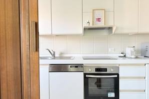 Cozinha com armários brancos, lava-louças, forno e cafeteira.