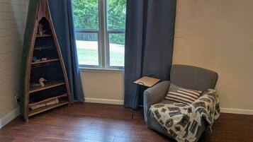 Une pièce avec une échelle en bois, un fauteuil gris, une petite table et une fenêtre avec des rideaux.