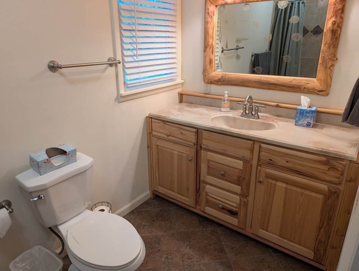 Een badkamer met toilet, wastafel, houten kastjes en een spiegel.