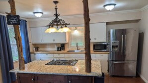 A kitchen with a central island, wooden cabinets, stainless steel appliances, and a chandelier. - Cozy Cottage Cabin #1 (Bull Shoals)
