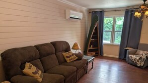 A living room with a brown sofa, a small table, a ladder, and a window with curtains. - Cozy Cottage Cabin #1 (Bull Shoals)